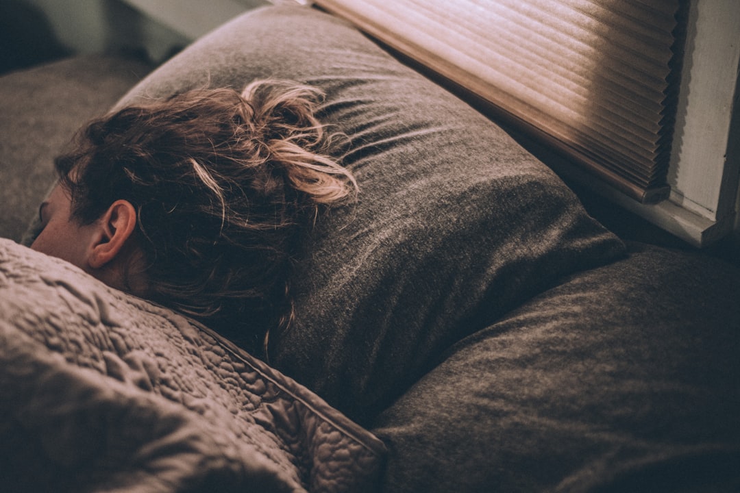 Woman sleeping under blankets in soft daylight, representing overnight recovery and sleep staging that rings and bands both measure