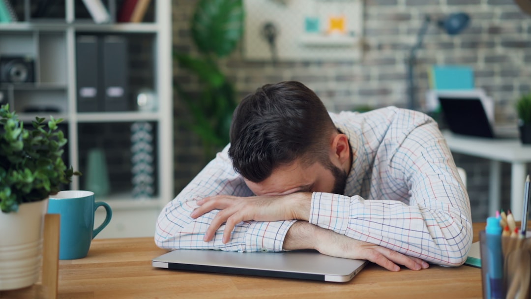 Man sitting at a desk with head in hands in front of a laptop, illustrating mental pressure that wearables infer from physiology