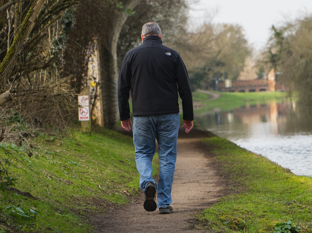 Person walking alone on a riverside path in daylight, showing calm movement that helps contextualize daytime recovery