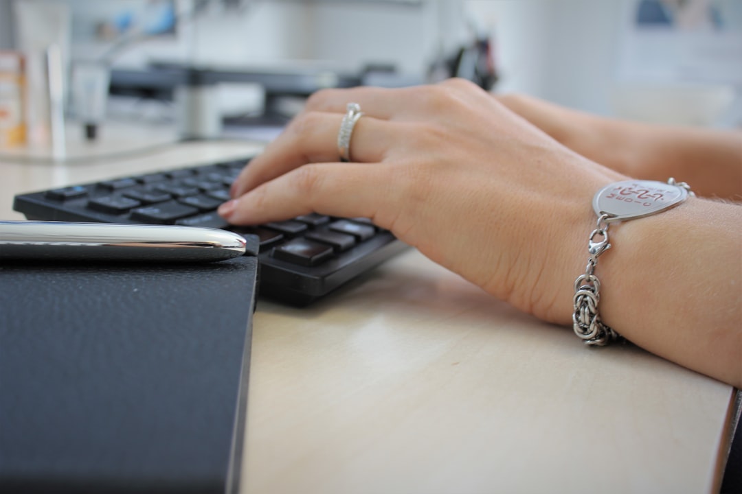 Close view of a hand with a silver ring typing on a black keyboard, showing everyday office strain tracked by wearables