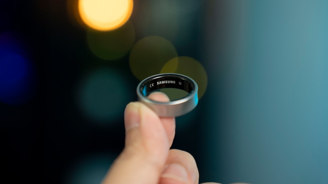 Hand holding a small smart ring above a desk, showing the compact sensor band buyers pay a subscription to unlock