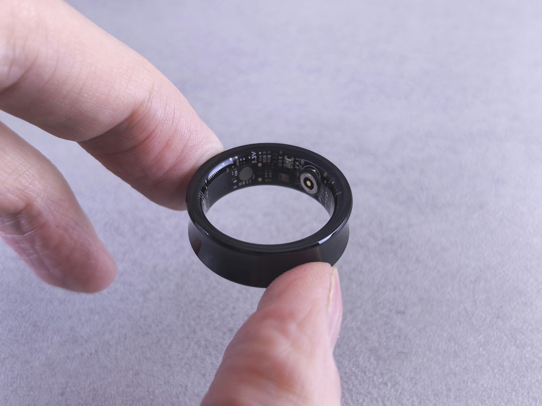 Fingers holding a black smart ring with visible circuit traces, illustrating the hardware already inside subscription locked wearables