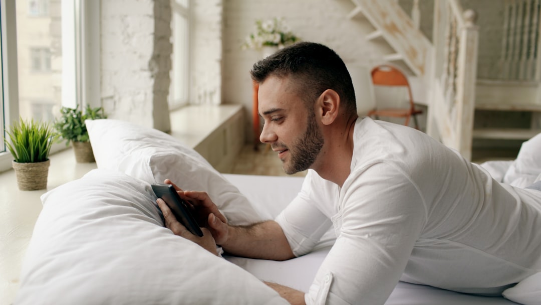Man lying in bed looking at phone in morning, checking sleep data before workout decision