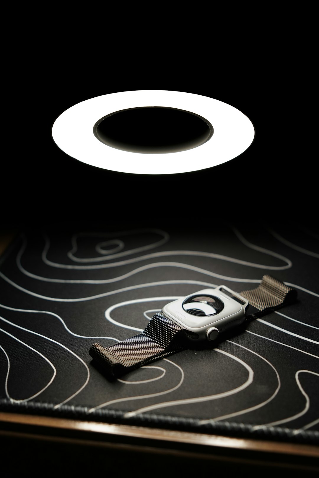 Smartwatch resting on patterned mat under bright ring light showing overnight charging routine for wearables