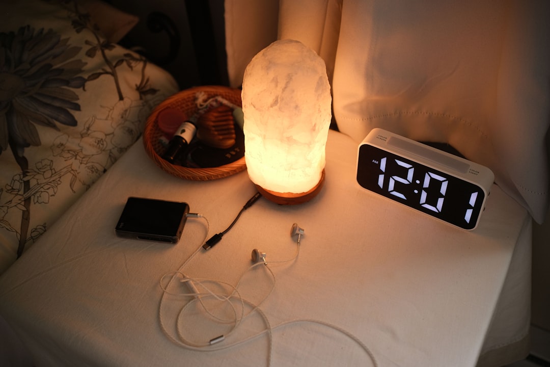 Bedside nightstand with lamp clock and chargers in dim evening light