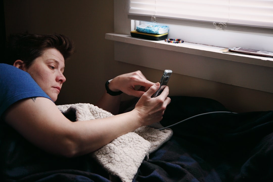 A person lying in bed checking their phone in a dark room, a common scene after a night of poor sleep