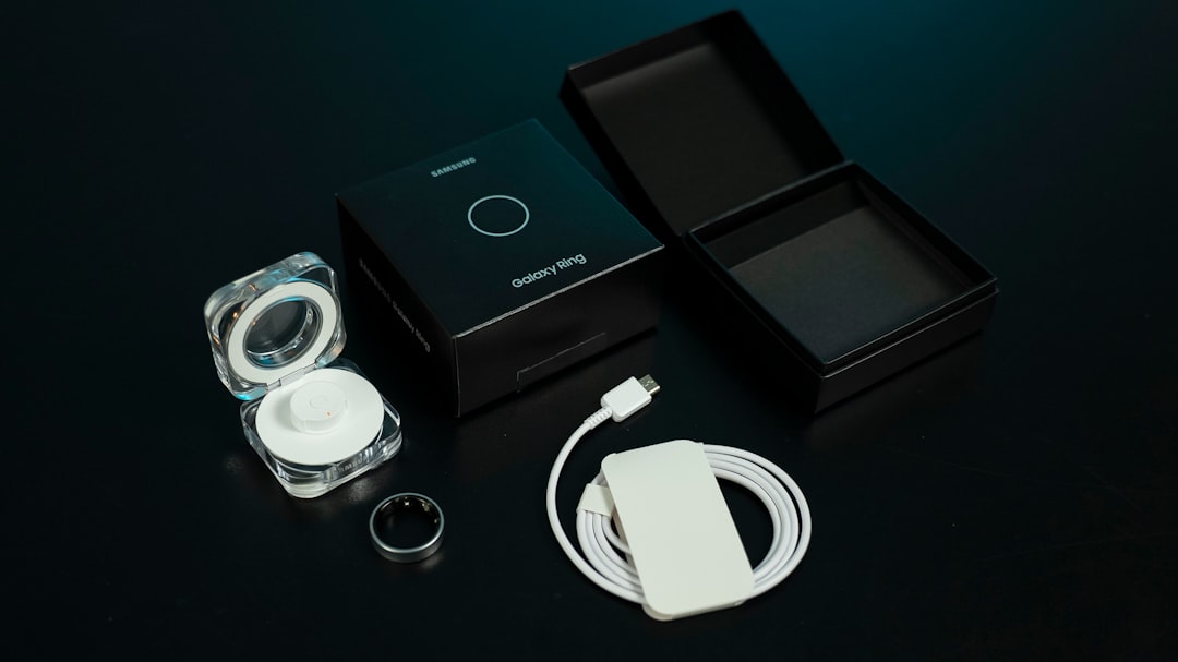 Hand holding a matte black smart ring next to its charging case, showing the inner sensor bumps that rest against finger skin