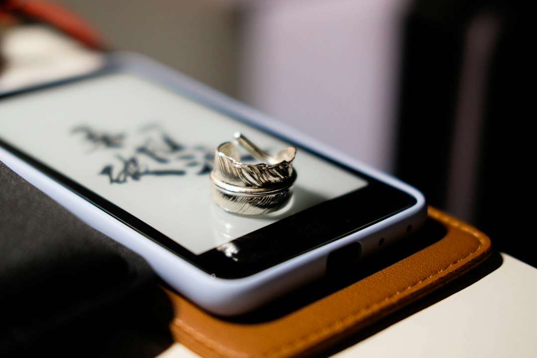 Silver smart ring resting on a white phone, showing the small size that forces shared charging designs