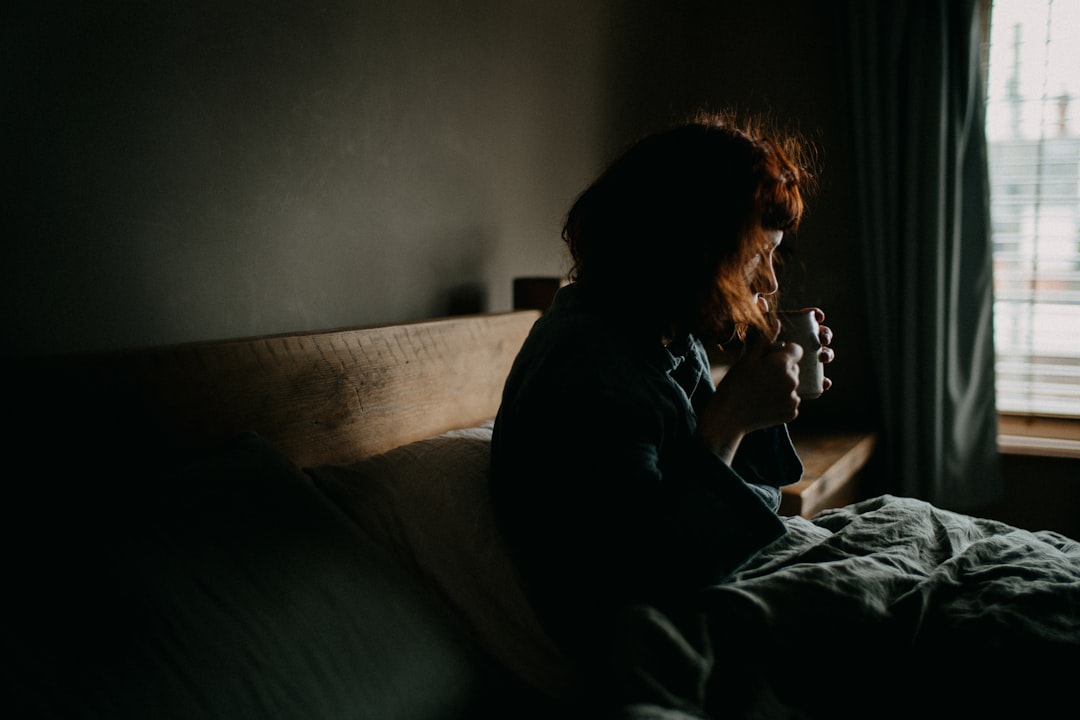 Woman sitting on bed beside bright morning window, checking her phone for the overnight summary after full sleep