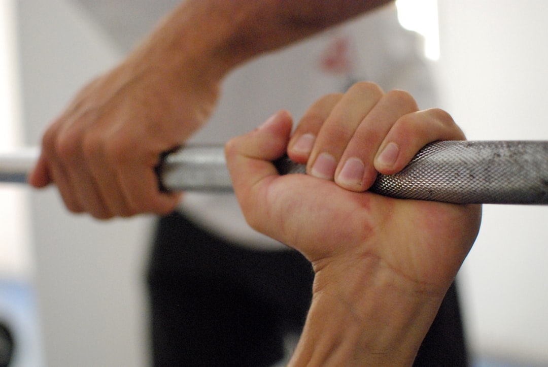 Hands gripping a barbell bar in a gym, illustrating grip pressure and finger motion that disrupts ring PPG signals