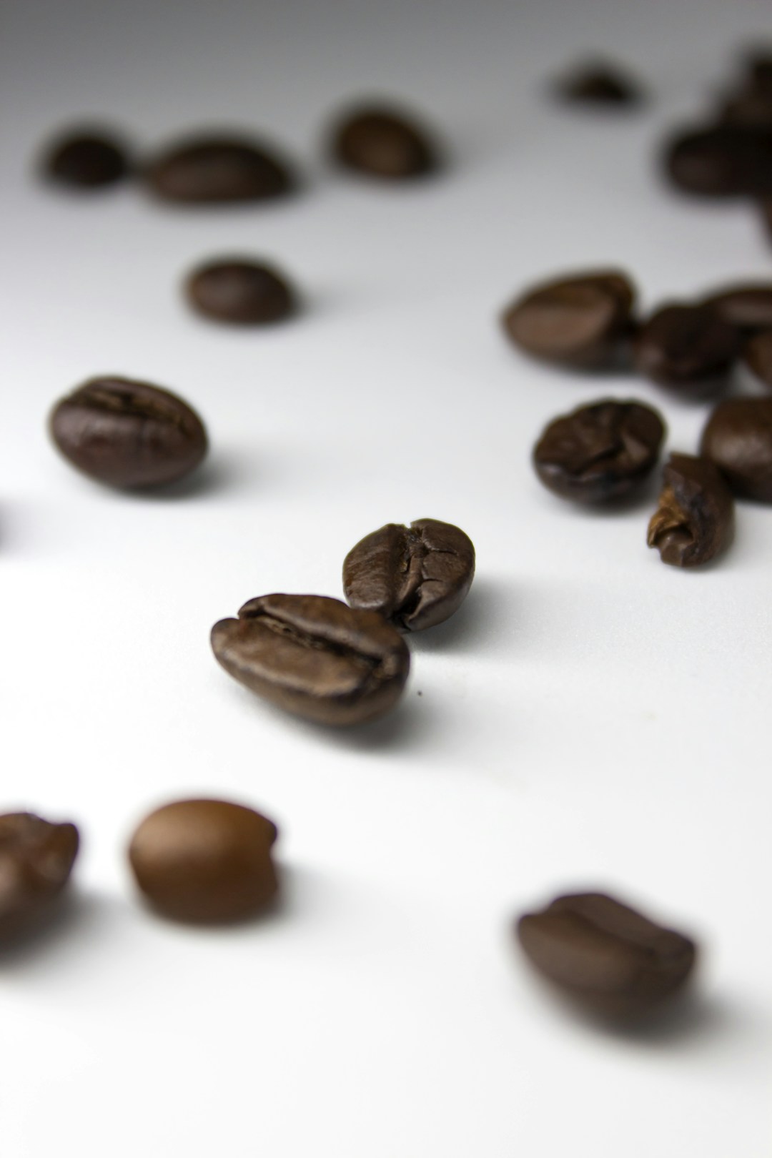 Closeup of roasted coffee beans scattered on a white surface, representing the source of caffeine that disrupts wearable biometric readings
